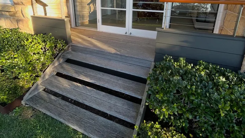 An old, weathered wooden deck with rotting boards, loose railings, and unsafe, worn-down stairs.