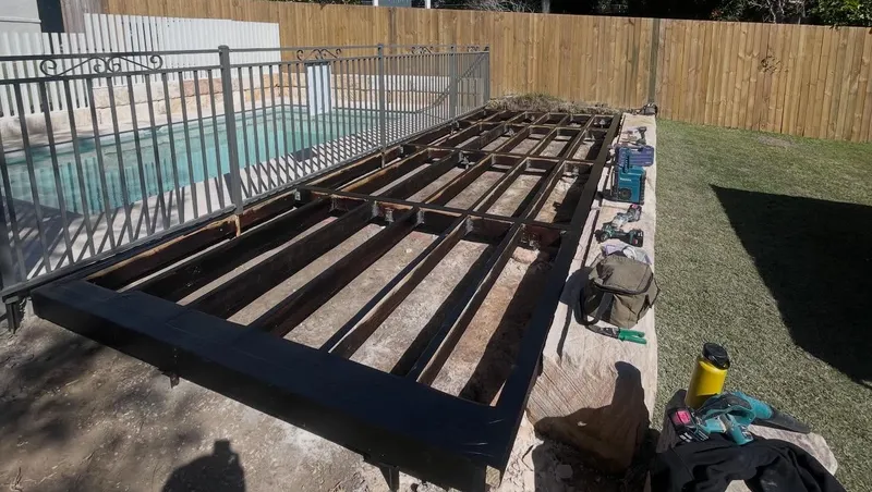 An open concrete pool surrounds area showing bare, unlandscaped ground prior to the new deck installation.